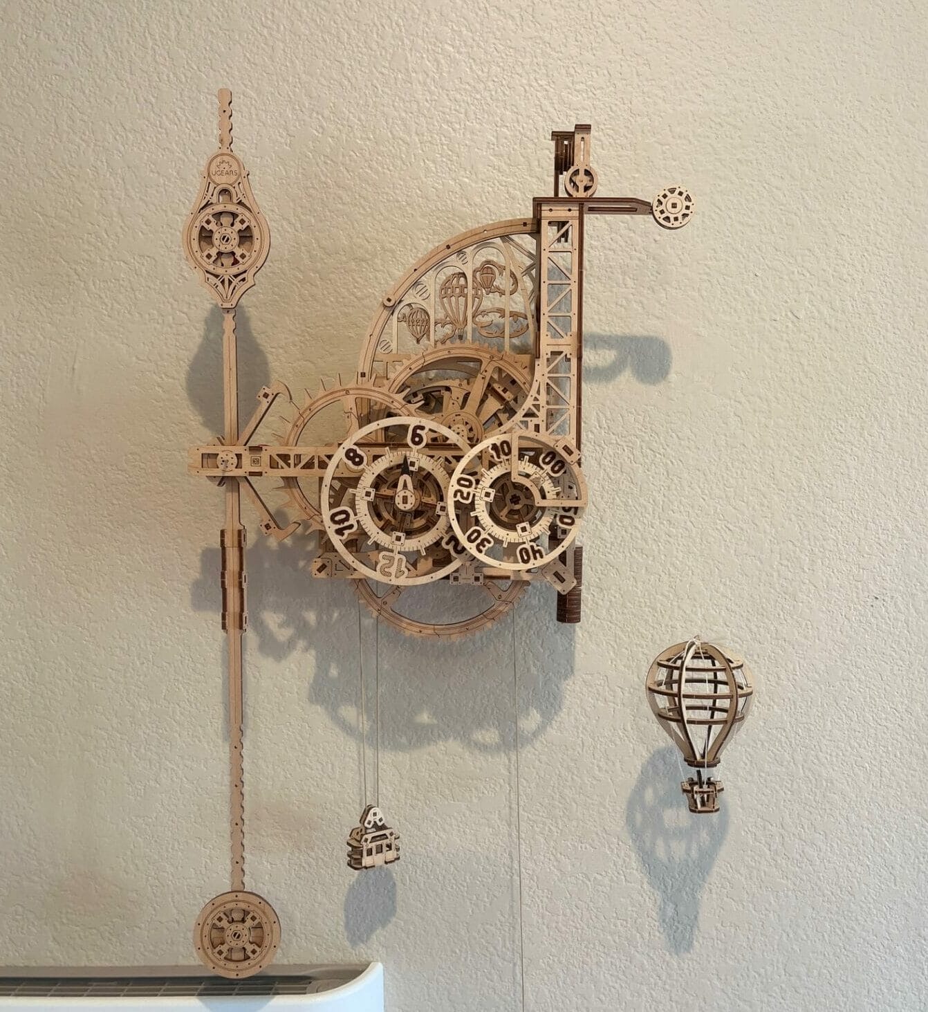 A wooden mechanical clock with intricate gears and a hanging airship decoration is mounted on a plain wall, offering a serene focal point perfect for fostering mental health and well-being.