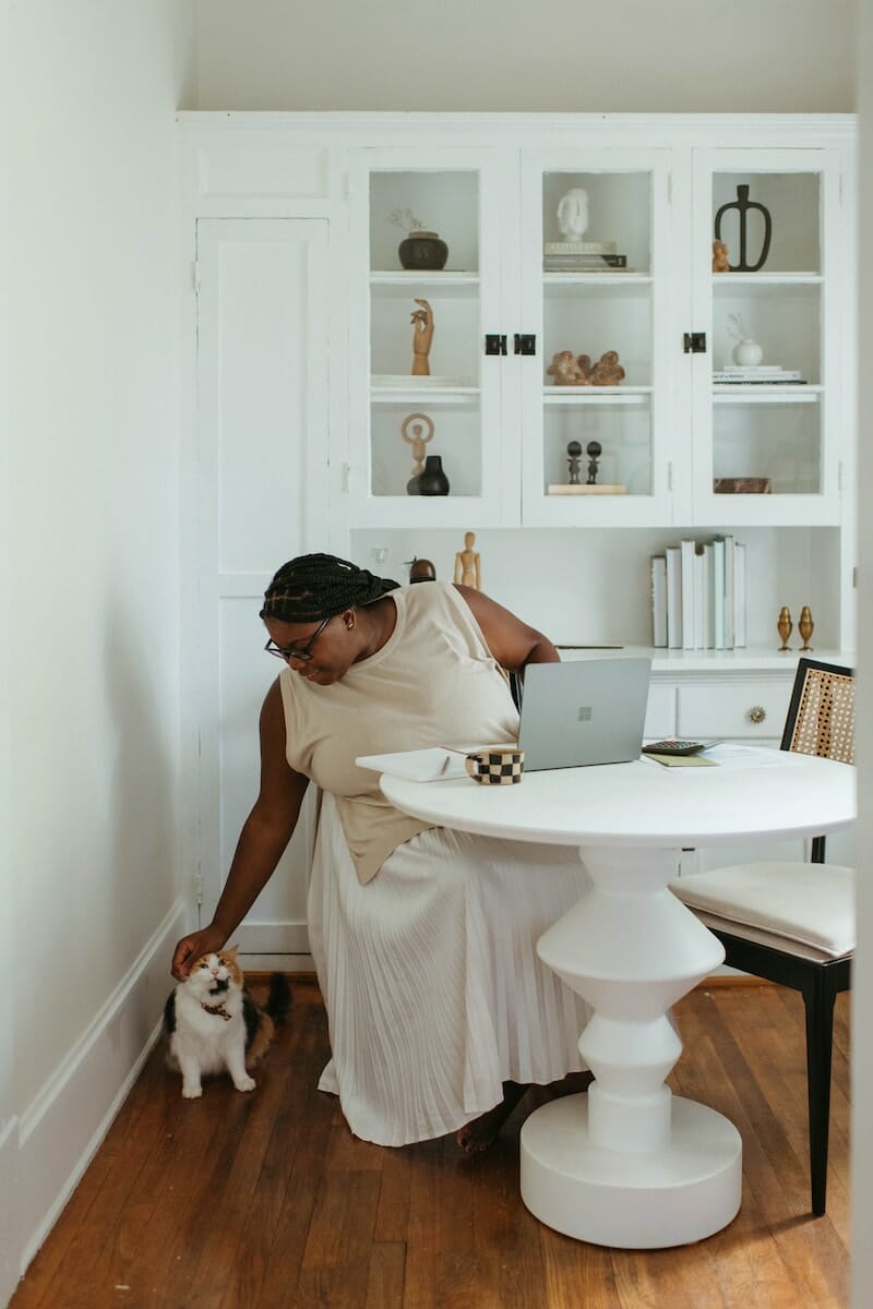 A woman sitting at a white table with a cat, emphasizing the importance of parenting for behavioral therapy.