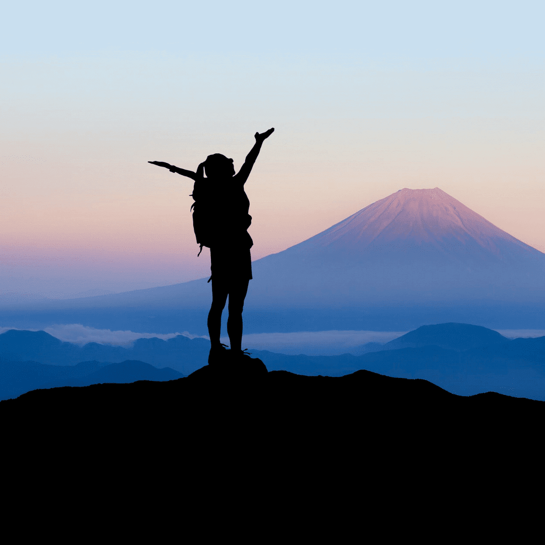 Silhouette of a hiker with a backpack raising arms triumphantly in front of mount fuji at sunrise.