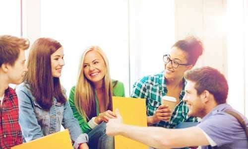 A group of five young adults engaging in a friendly conversation, sitting and smiling in a brightly lit room.