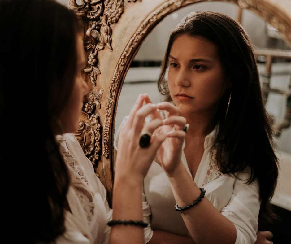 A woman applying makeup while looking into an ornate mirror.